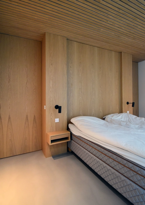 Indretning til soveværelse med væg som sengegavl i egetræ og speciallavet sengebord i egetræ